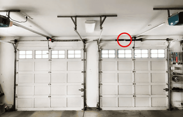 A close-up of two closed garage doors reveals a break in one of the torsion springs above the right door, highlighted by a red circle. It's essential to seek professional garage door repair to ensure safety and functionality.