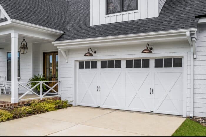 White garage with carriage-style doors and driveway, attached to a house with a covered porch and decorative lighting.